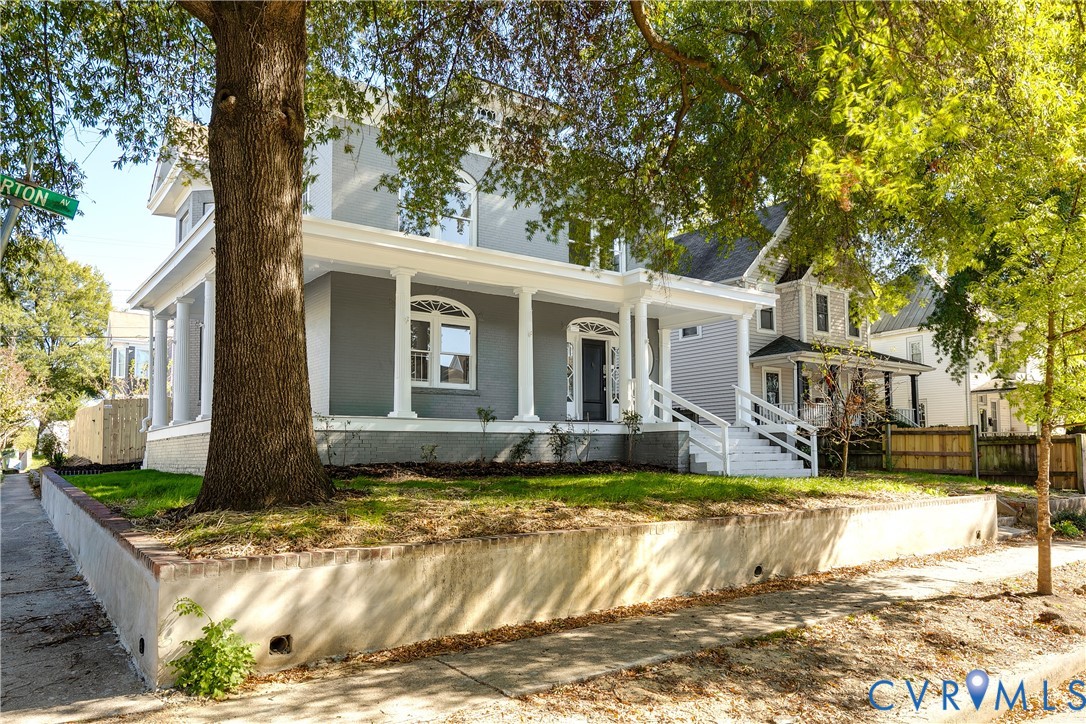 Two-story residence featuring a covered wrap-around porch, classical columns, arched windows, and a raised concrete retaining wall