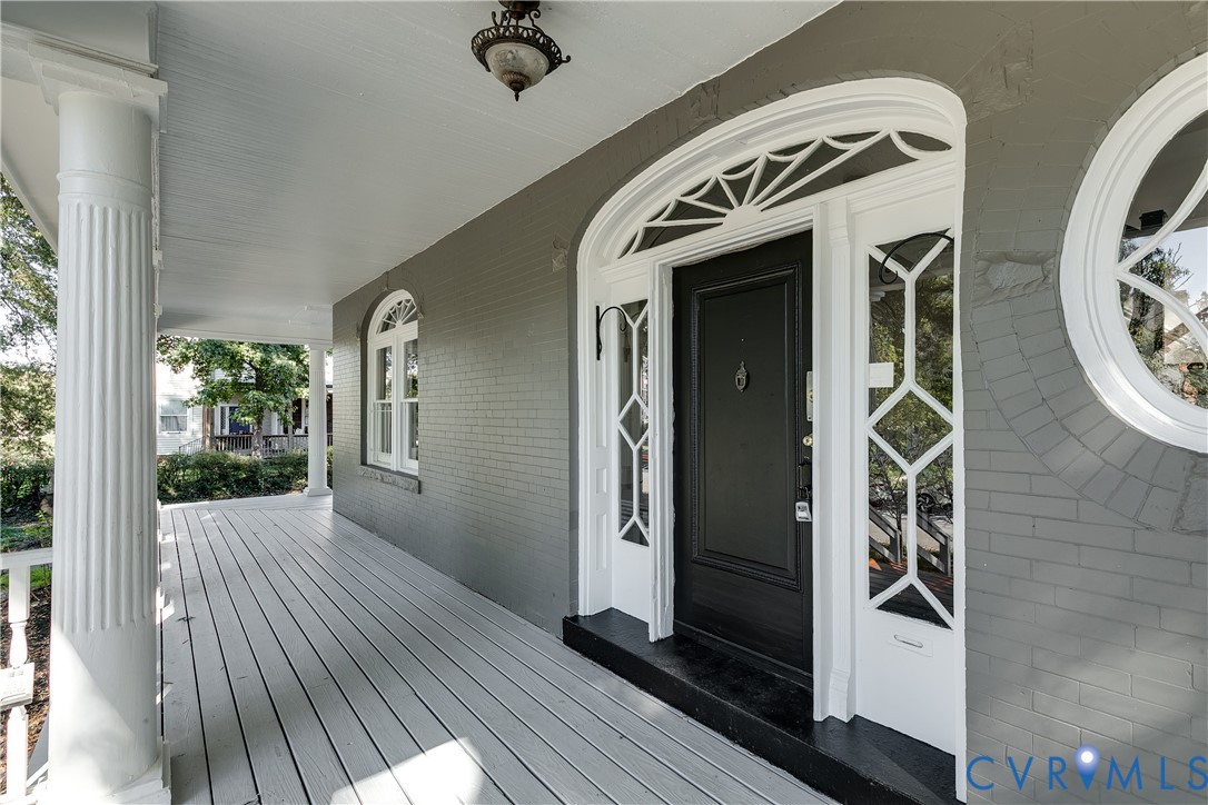 Covered front porch featuring fluted columns, brick exterior, arched entryway with decorative fanlight transom, sidelights with geometric mullions, and circular accent window