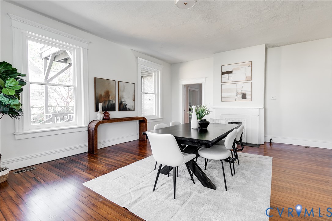 Dining area featuring wood-finish flooring, two large windows with crisp white casing, and a built-in fireplace mantel