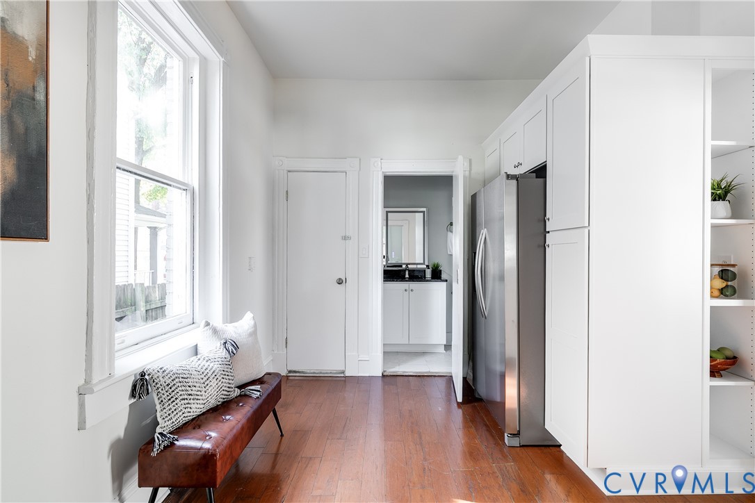 Wood-finish flooring, custom white cabinetry, stainless steel refrigerator, and large window with natural light