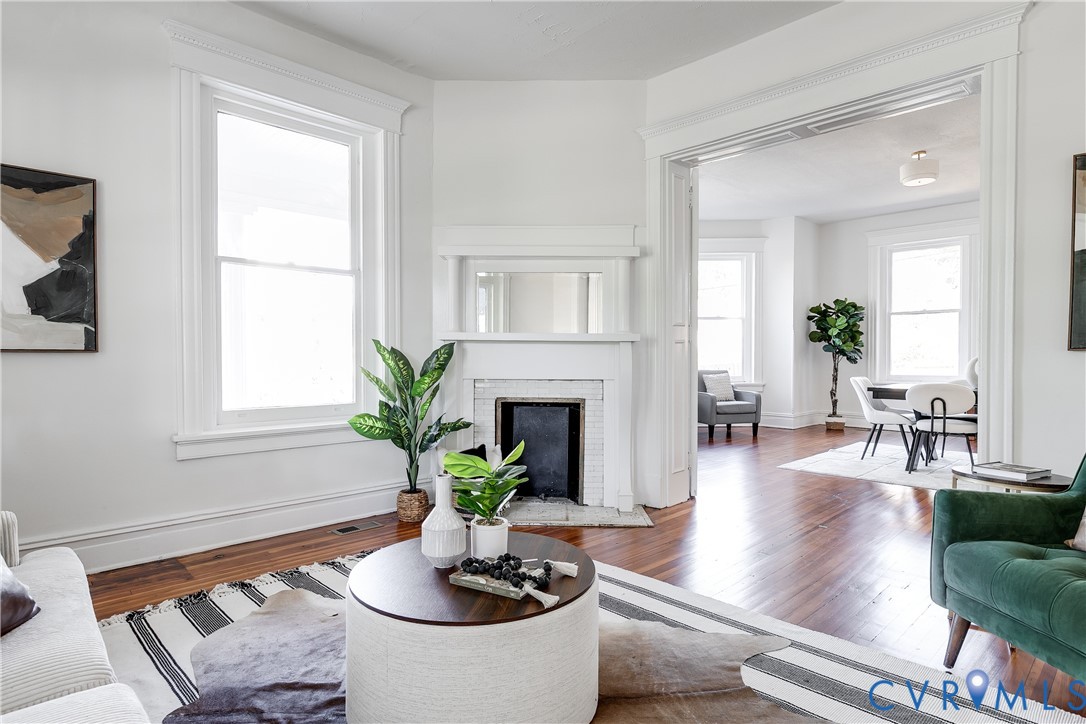 Living area featuring hardwood flooring, a fireplace with a mantel and mirror, tall windows with millwork casing, and crown molding