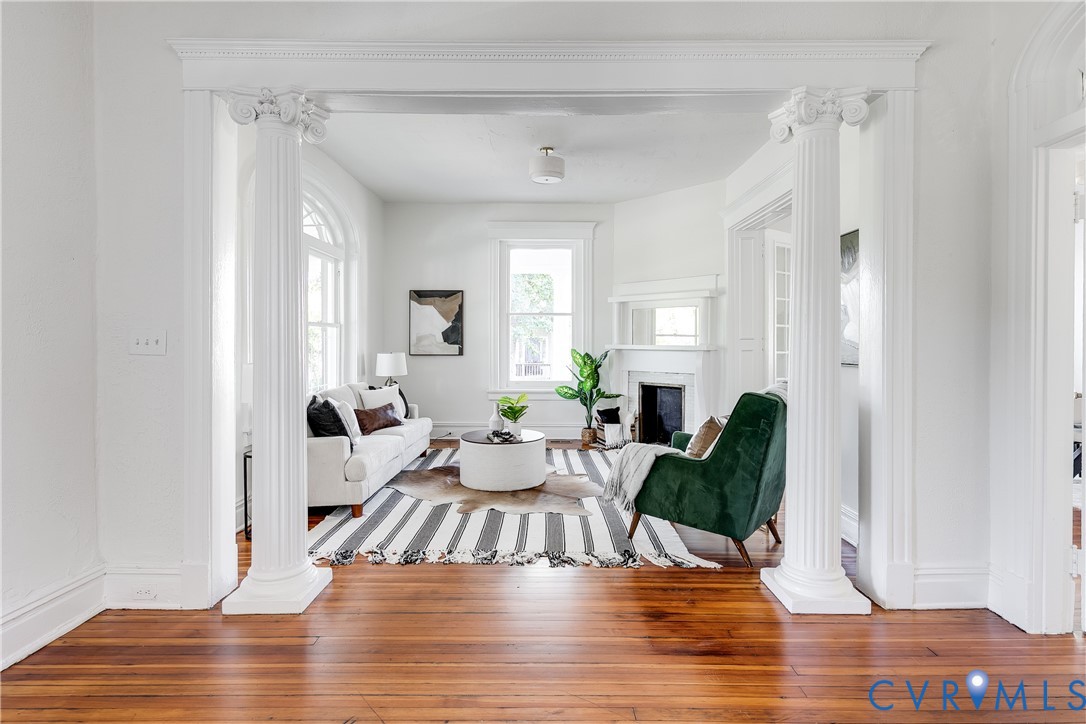 Living area featuring fluted Ionic columns, wood-finish flooring, arched window detailing, and a fireplace with a mantel