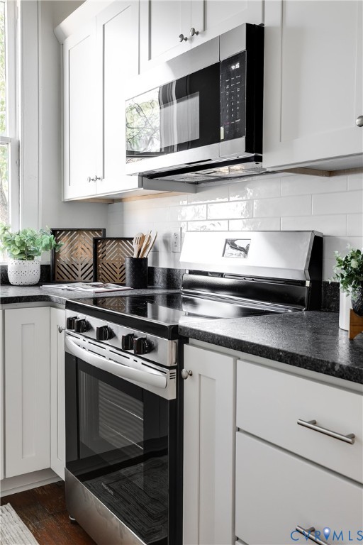 White shaker-style cabinetry, dark stone countertops, stainless steel electric range, over-the-range microwave, and white subway tile backsplash
