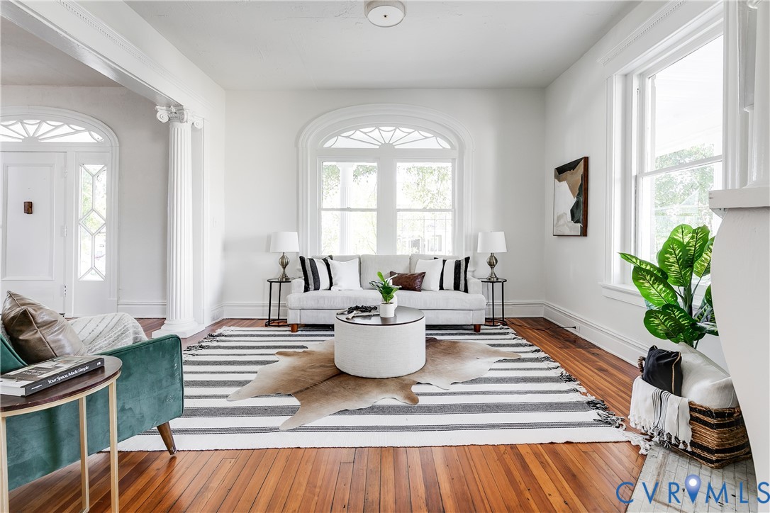 Living area featuring wood-finish flooring, an arched window with detailed fanlight, and a classic fluted column