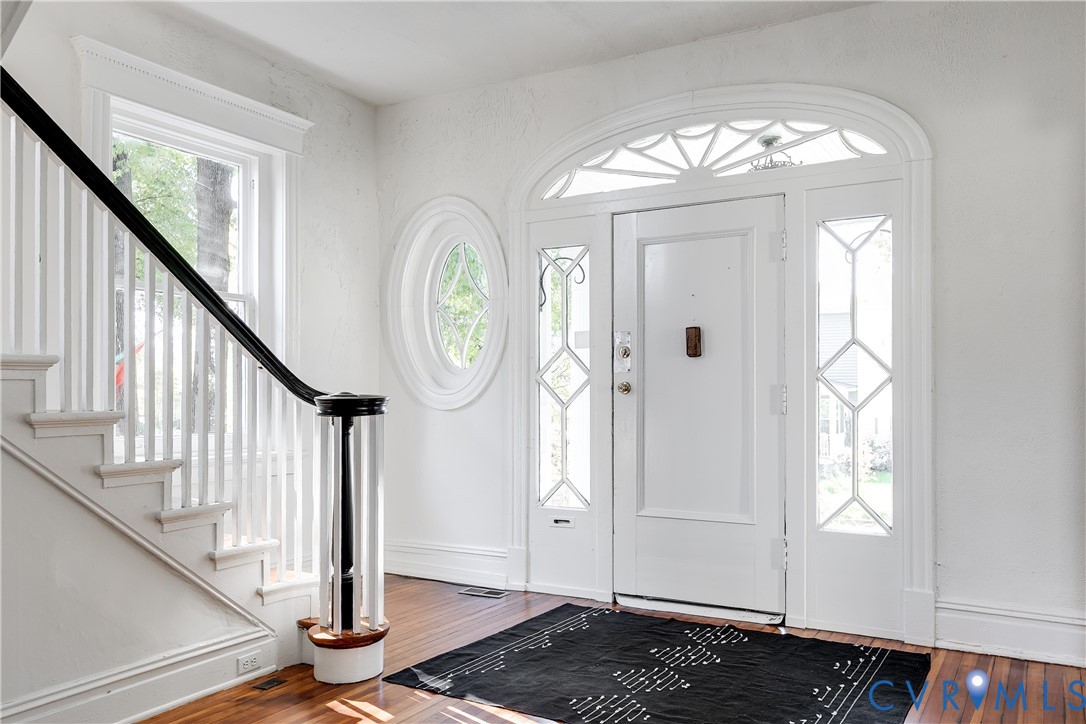 Foyer featuring wood-finish flooring, a decorative arched transom window, a round accent window, and a staircase with a contrasting black handrail
