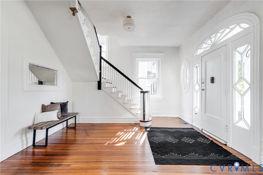 Foyer featuring wood-finish flooring, a white front door with decorative glass sidelights and transom, and a staircase with white spindles and a dark handrail