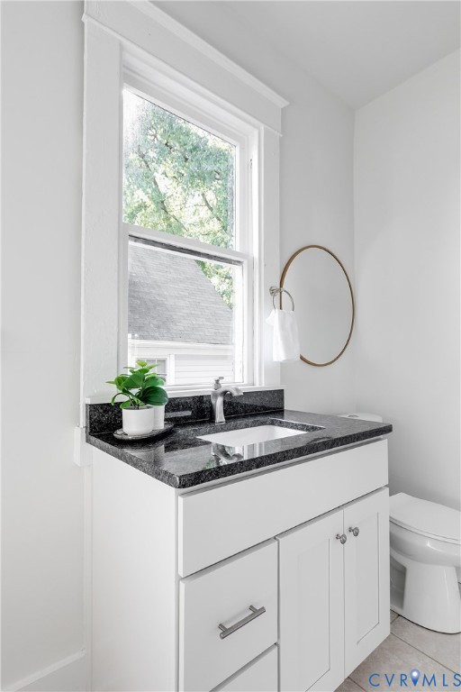 White shaker-style cabinetry with a dark stone countertop, integrated rectangular sink, brushed metal faucet, and tall window with wide trim