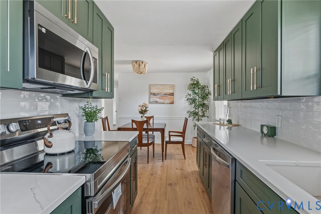 Modern kitchen featuring green shaker-style cabinetry, stainless steel appliances, white subway tile backsplash, and light-toned countertops