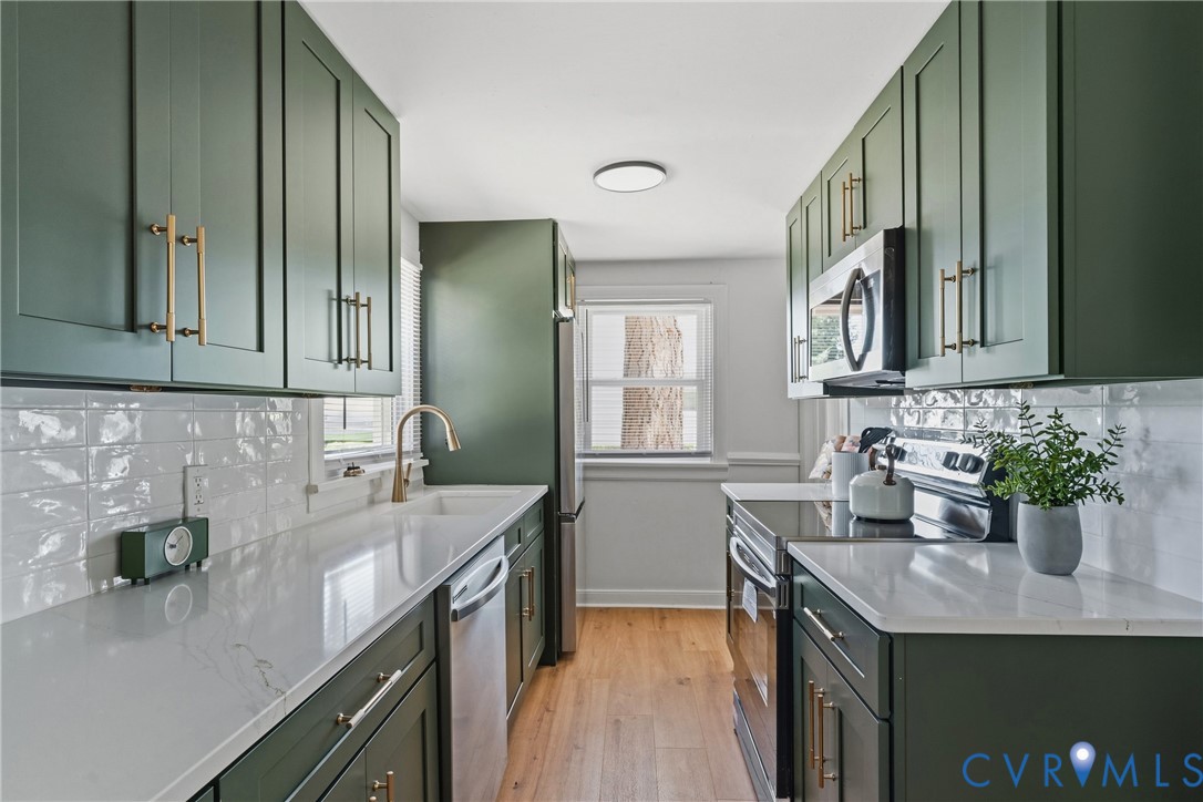 Galley kitchen with dark green cabinetry, white textured subway tile backsplash, white countertops, and wood-finish flooring