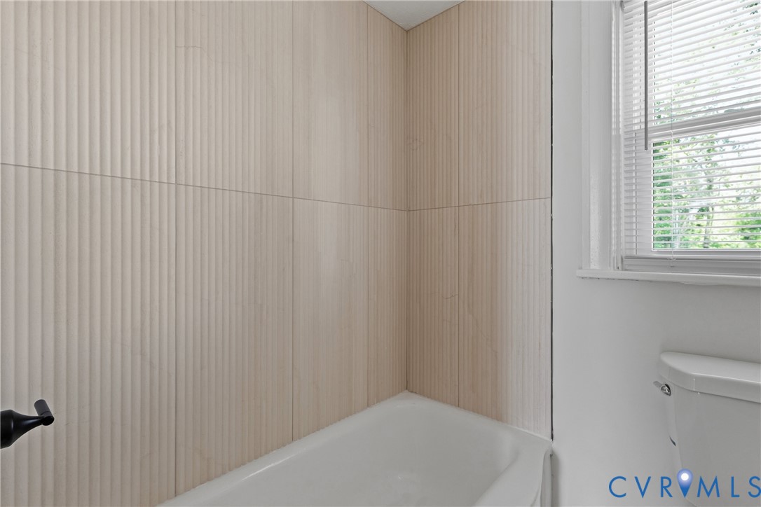 Bathtub with textured wall tiling and an adjacent window with blinds