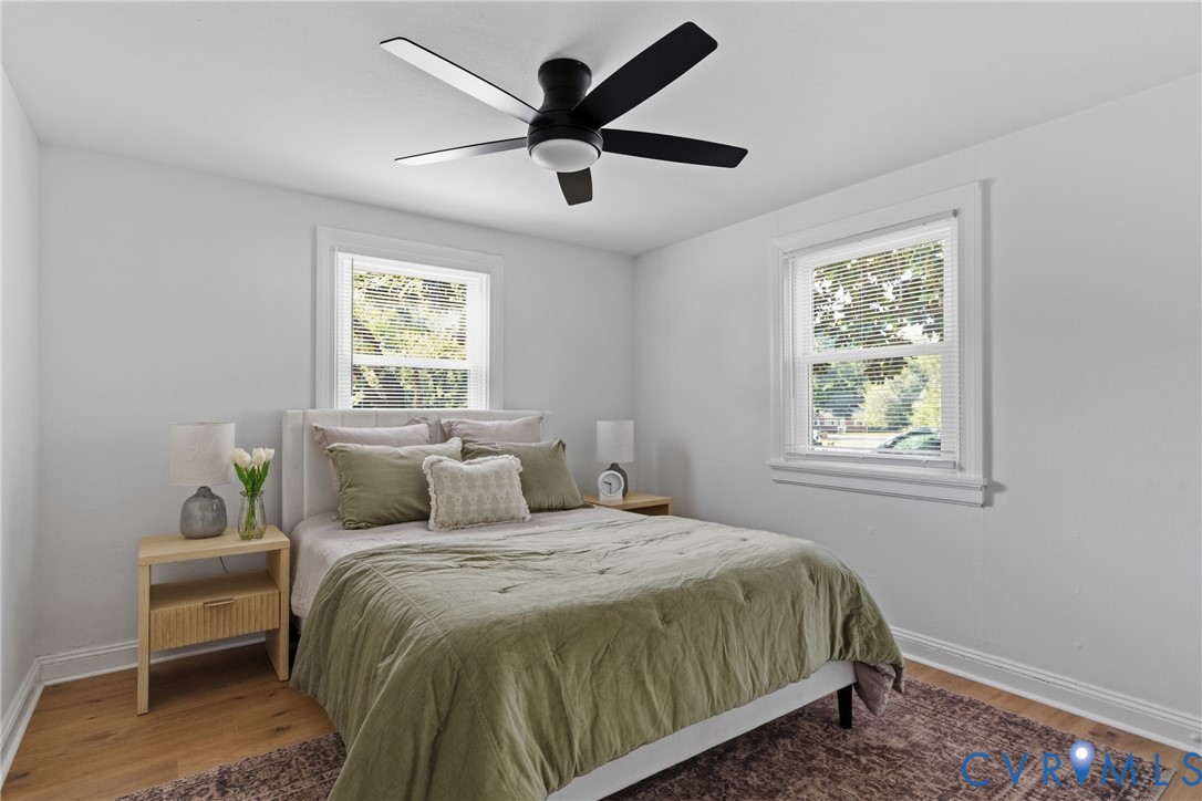 Light-filled room featuring two windows, a ceiling fan with integrated lighting, and wood-finish flooring