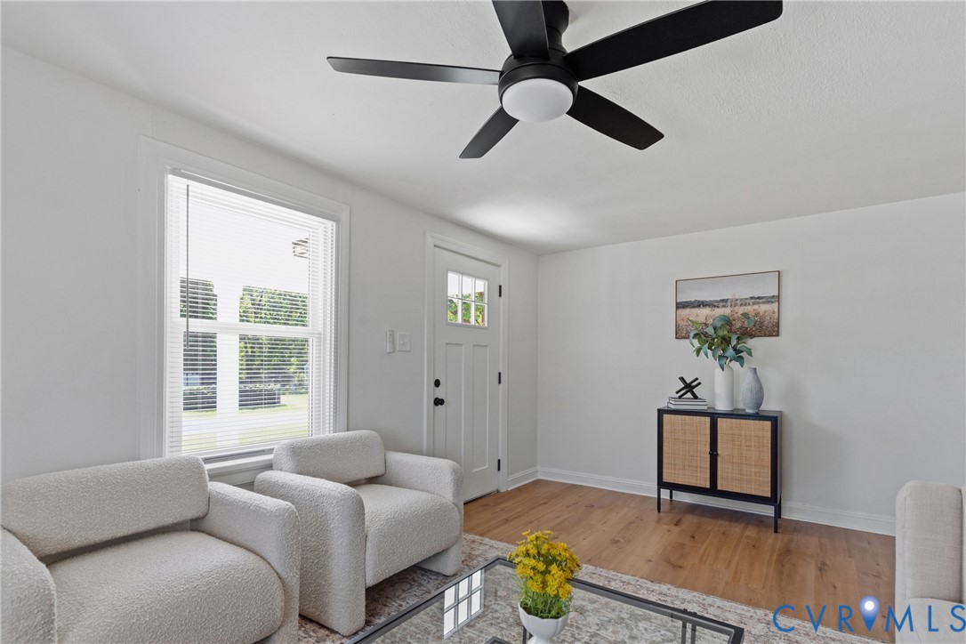 Bright interior with wood-finish flooring, a white paneled entry door with glass inserts, and a black ceiling fan with an integrated light