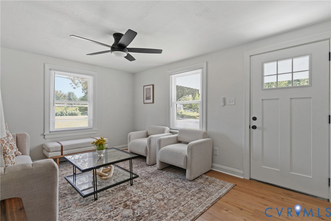 Wood-finish flooring, white paneled door with glass inserts, two windows with white trim, ceiling fan with integrated lighting, and light-colored walls Wood-finish flooring, white paneled door with glass inserts, two windows with white trim, ceiling fan with integrated lighting, and light-colored walls