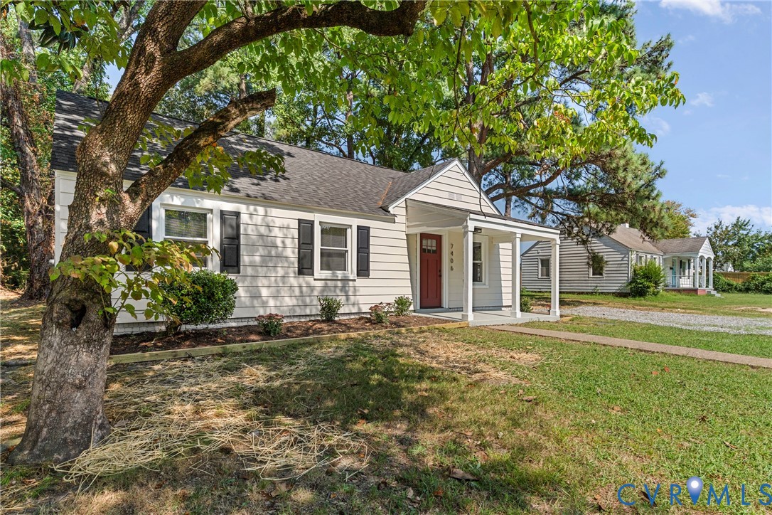 White siding exterior with black window shutters, a red entry door, a covered porch, and a paved driveway White siding exterior with black window shutters, a red entry door, a covered porch, and a paved driveway