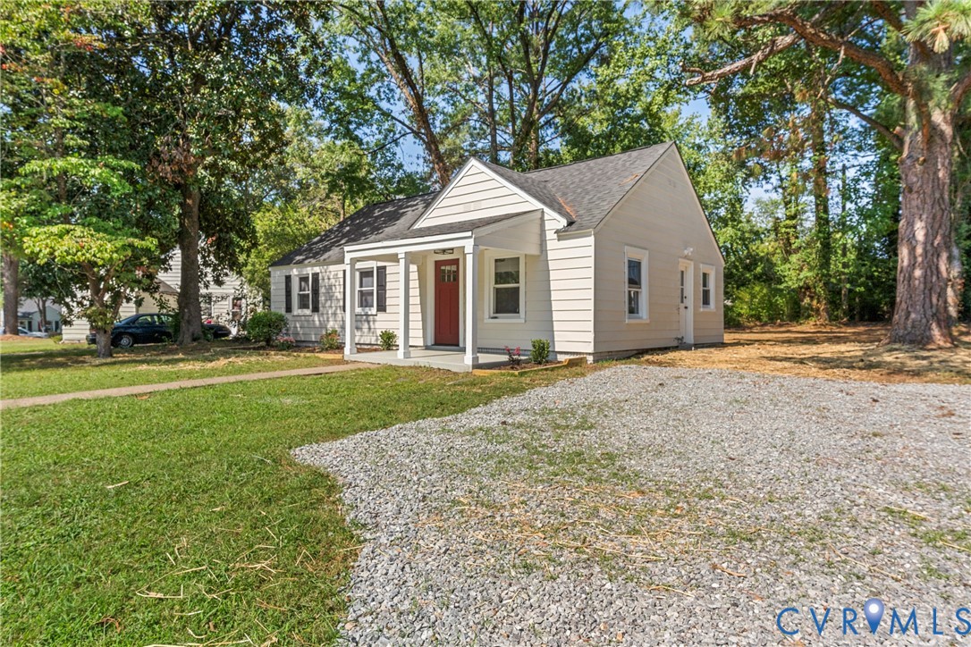 Light-colored siding exterior with a red front door, covered porch, dark roof, and a gravel driveway