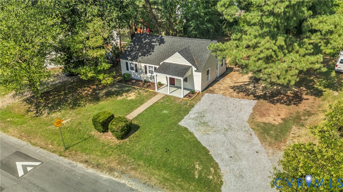 Cottage-style residence featuring a covered front porch, gravel driveway, and mature landscaping