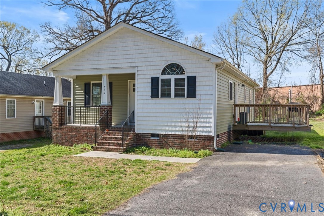 Exterior featuring a brick foundation, shake siding, covered front porch with tapered columns, arched window detailing, and an attached side deck