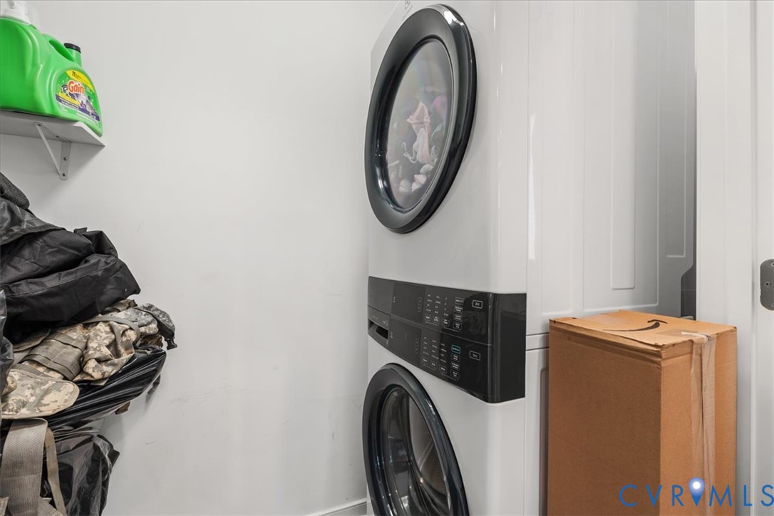 Stackable white front-load washer and dryer unit with black digital interface panels, accompanied by a fixed wall-mounted storage shelf