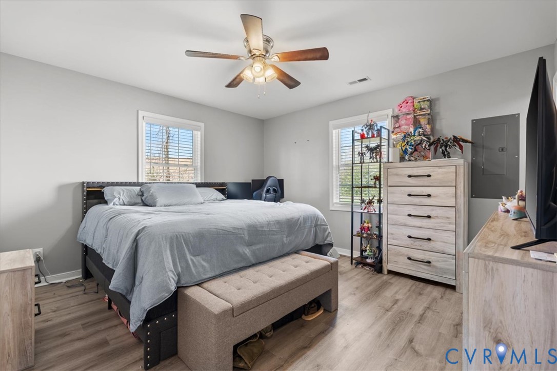 Room featuring neutral-toned walls, wood-finish flooring, two windows, and a ceiling fan with integrated light fixture