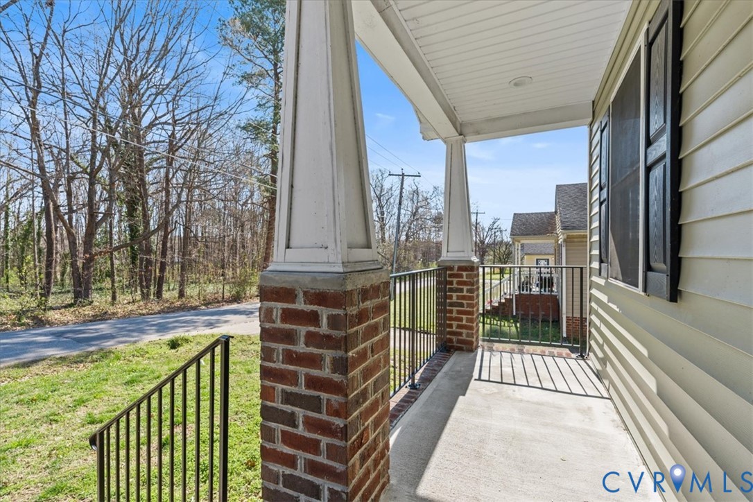 Covered porch featuring concrete flooring, brick-based columns with tapered pedestals, and black metal railings
