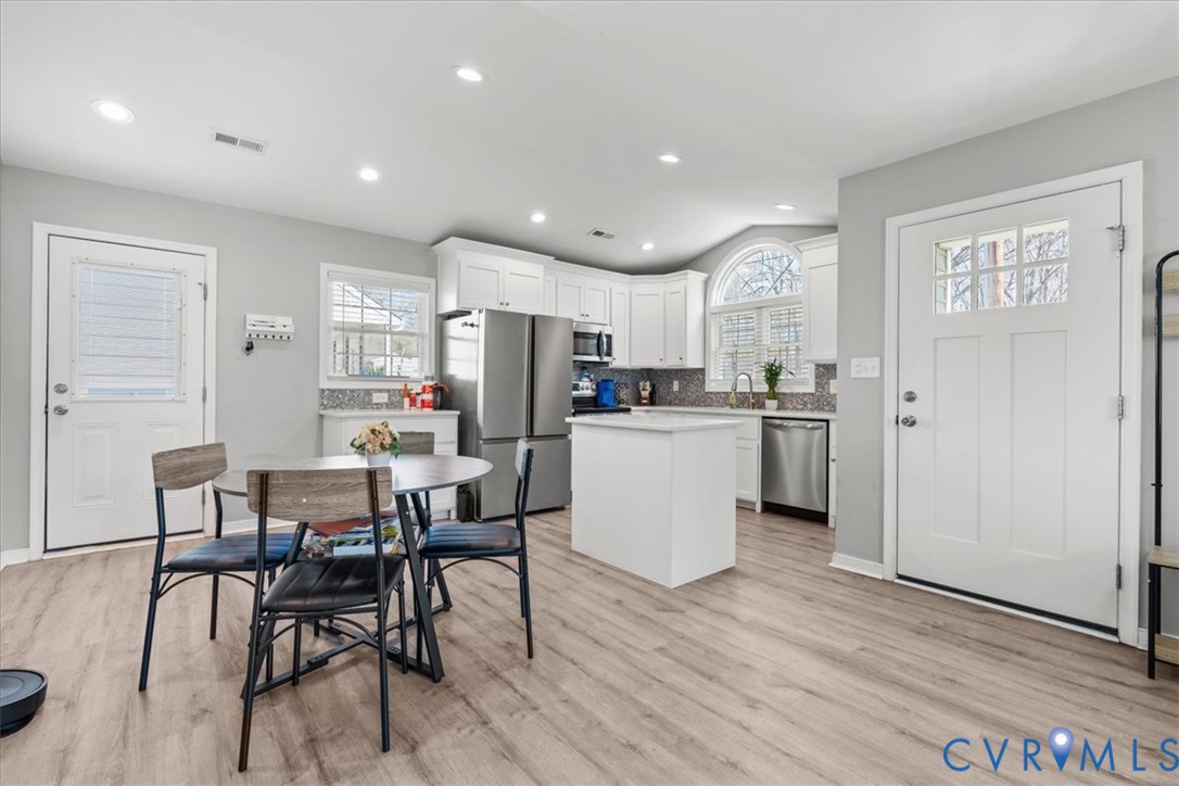 Kitchen featuring white cabinetry, stainless steel appliances, a central island with a solid-surface countertop, arched window, and wood-finish flooring