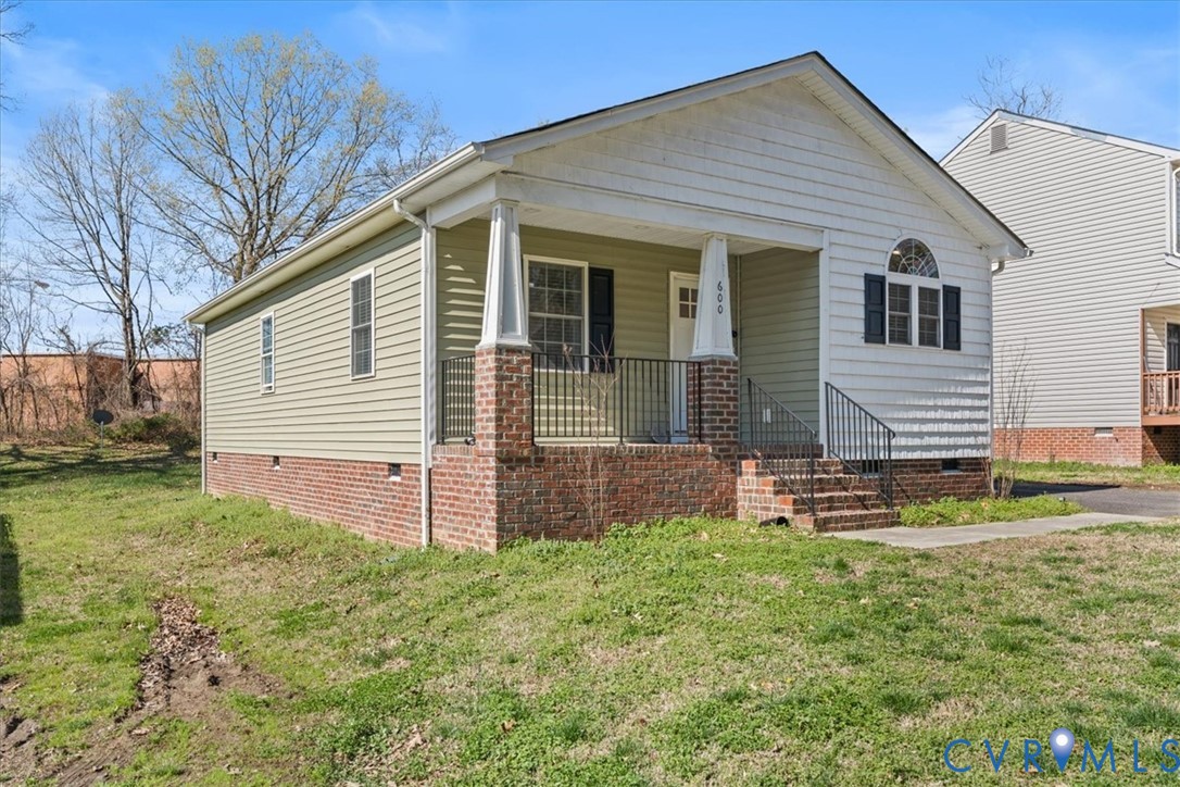 Single-story residence featuring horizontal siding, a brick foundation, a covered front porch with tapered columns, and arched decorative window detailing