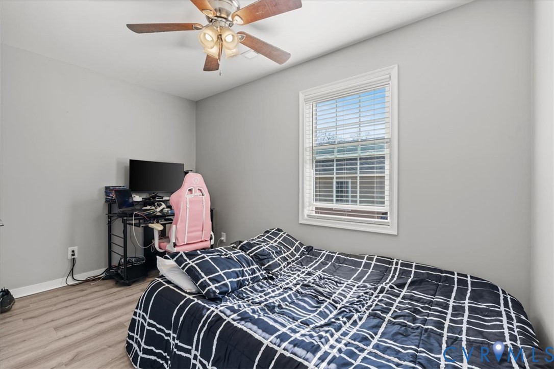 Neutral interior room featuring wood-finish flooring, a ceiling fan with integrated lighting, and a window with horizontal blinds