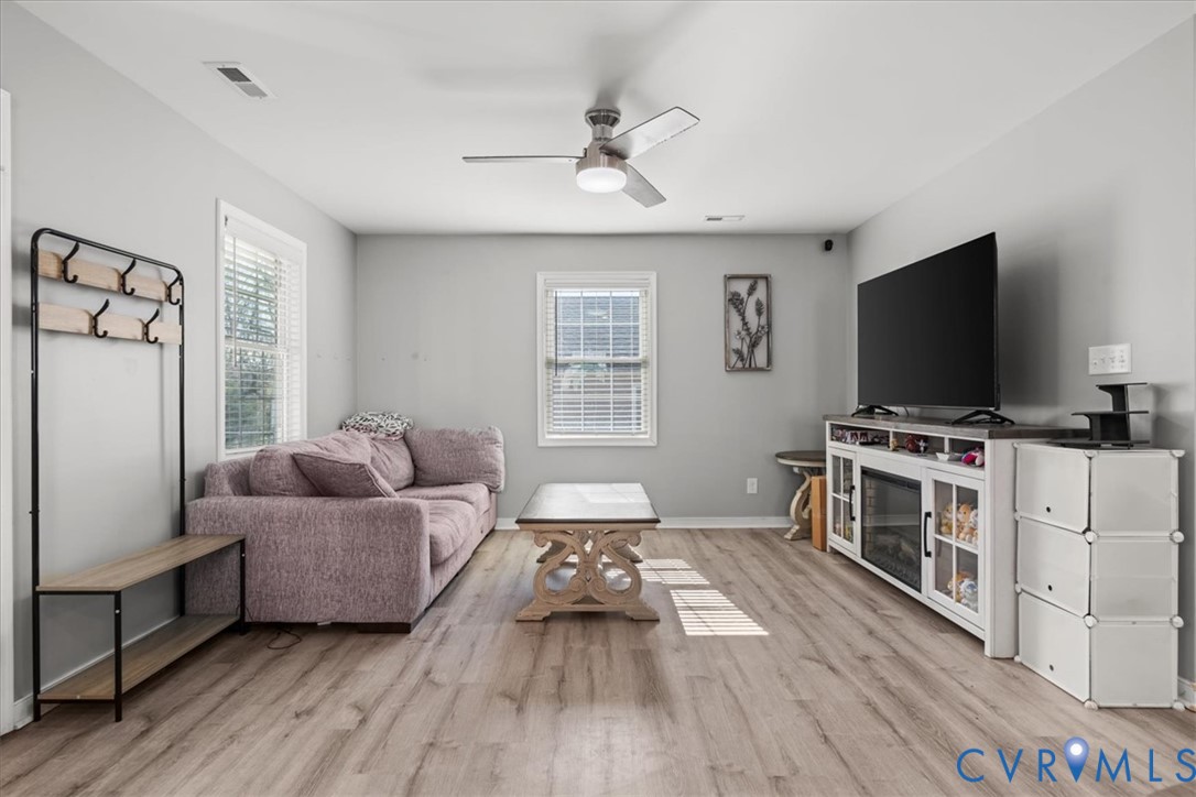 Neutral-toned interior featuring wood-finish flooring, dual windows with blinds, and a brushed nickel ceiling fan with integrated lighting