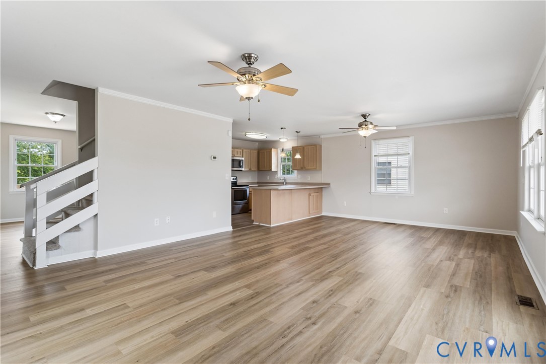 Open interior featuring wood-finish flooring, two ceiling fans, multi-pane windows, and a kitchen peninsula with integrated cabinetry Open interior featuring wood-finish flooring, two ceiling fans, multi-pane windows, and a kitchen peninsula with integrated cabinetry