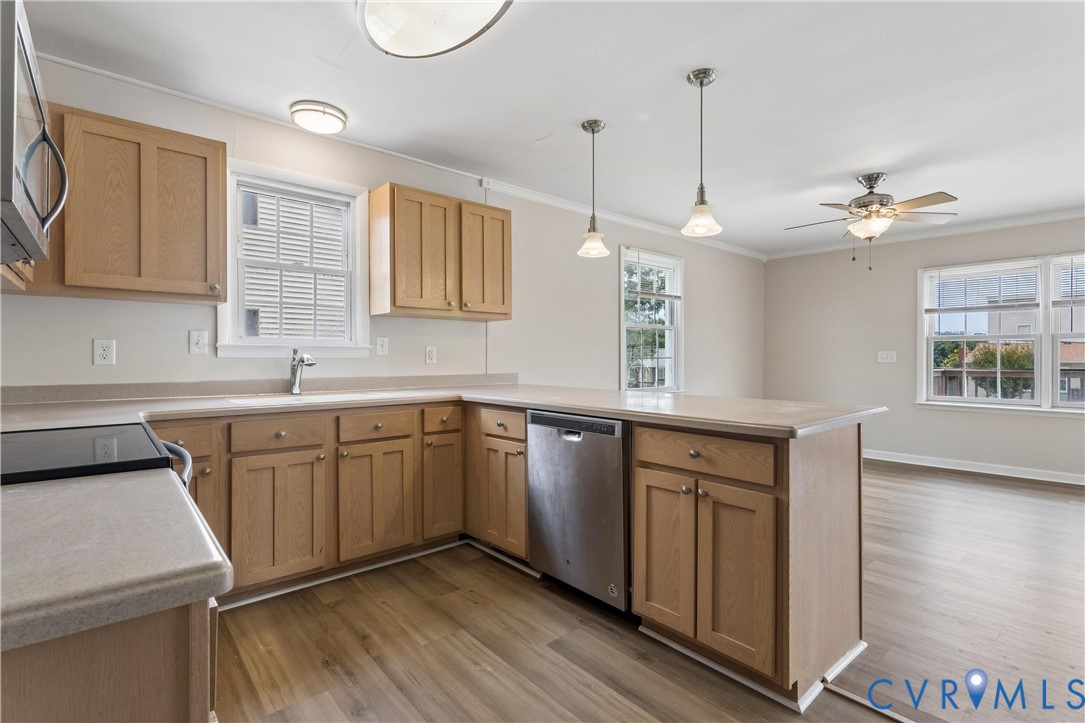 Kitchen featuring wood cabinetry, stainless steel dishwasher, wood-finish flooring, dual pendant lighting, and a peninsula countertop