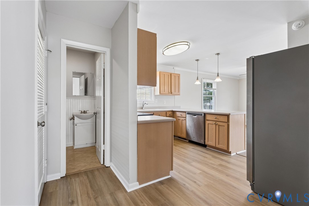Kitchen featuring wood-finish cabinetry, stainless steel dishwasher, and neutral countertops, complemented by wood-finish flooring and pendant lighting