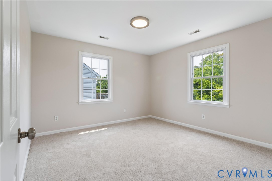 Neutral-toned room featuring neutral carpeting, double-hung windows with grid muntins, and a flush-mount circular ceiling fixture