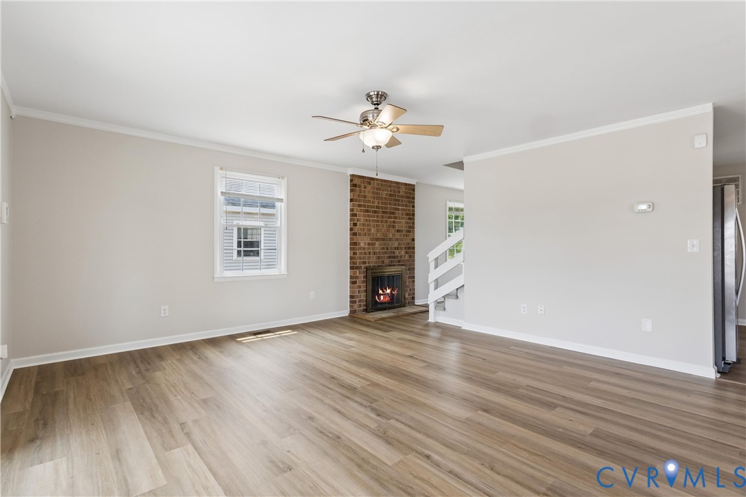Interior space featuring wood-finish flooring, a floor-to-ceiling brick fireplace, ceiling-mounted fan, multi-pane window, and white handrail staircase Interior space featuring wood-finish flooring, a floor-to-ceiling brick fireplace, ceiling-mounted fan, multi-pane window, and white handrail staircase