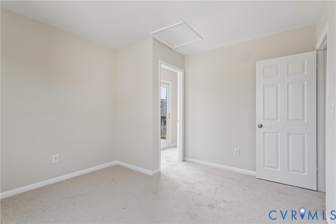 Neutral-toned interior space featuring wall-to-wall carpeting, a six-panel door, and an integrated ceiling access panel