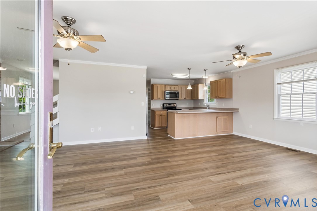 Open-concept living space featuring wood-finish flooring, recessed lighting, dual ceiling fans, and a kitchen equipped with wood cabinetry and a peninsula counter Open-concept living space featuring wood-finish flooring, recessed lighting, dual ceiling fans, and a kitchen equipped with wood cabinetry and a peninsula counter