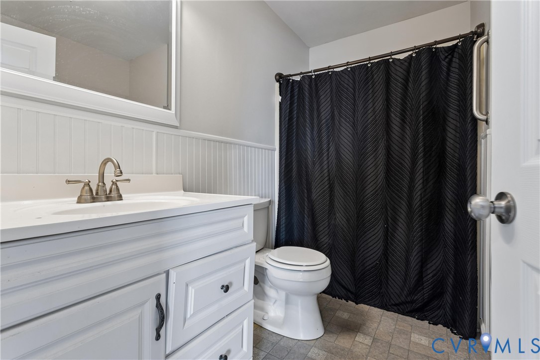 Bathroom featuring a white vanity with integrated basin, beadboard wall paneling, framed wall mirror, and neutral tile flooring