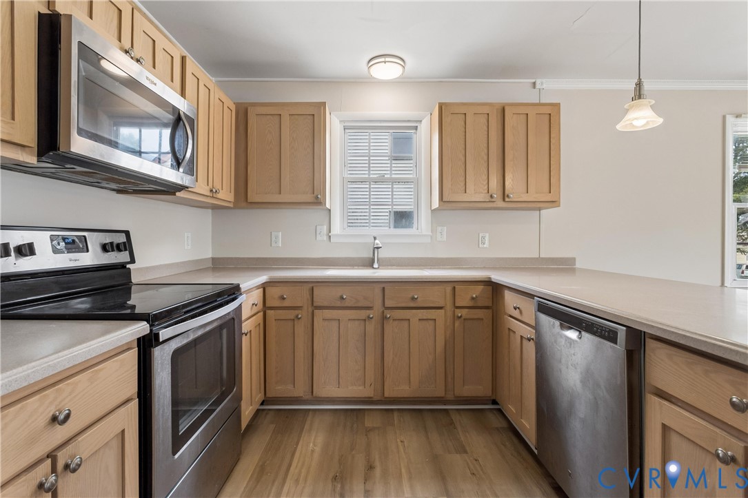 Kitchen featuring light-finish cabinetry, neutral solid-surface countertops, stainless steel appliances, wood-finish flooring, and a pendant light fixture