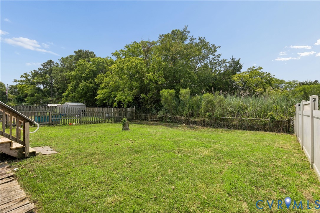 Rear yard featuring a grass lawn, perimeter wood fencing, a white vinyl privacy fence, and mature trees