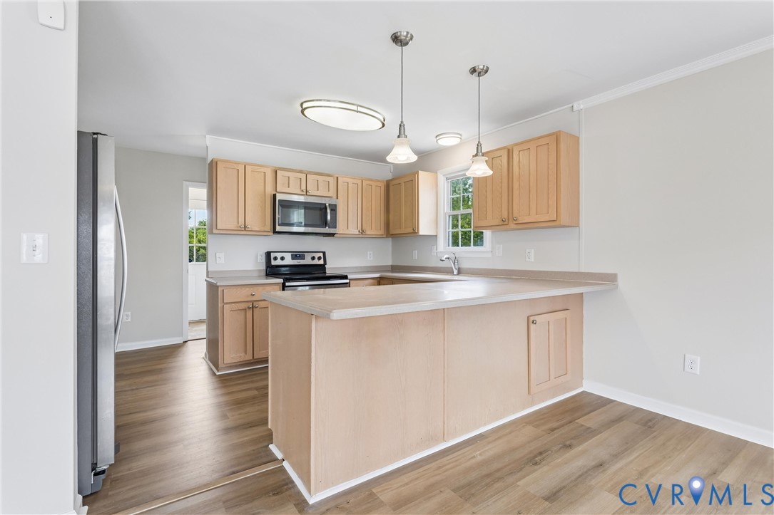 Kitchen featuring light-finish cabinetry, a peninsula countertop, stainless steel appliances, dual pendant lighting, and wood-finish flooring