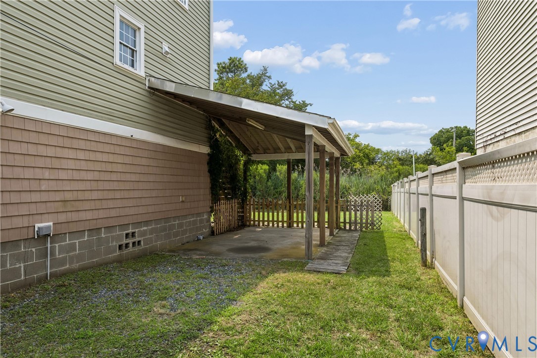 Covered concrete patio with overhead support structure, vinyl siding, decorative shingle accents, and perimeter vinyl fencing