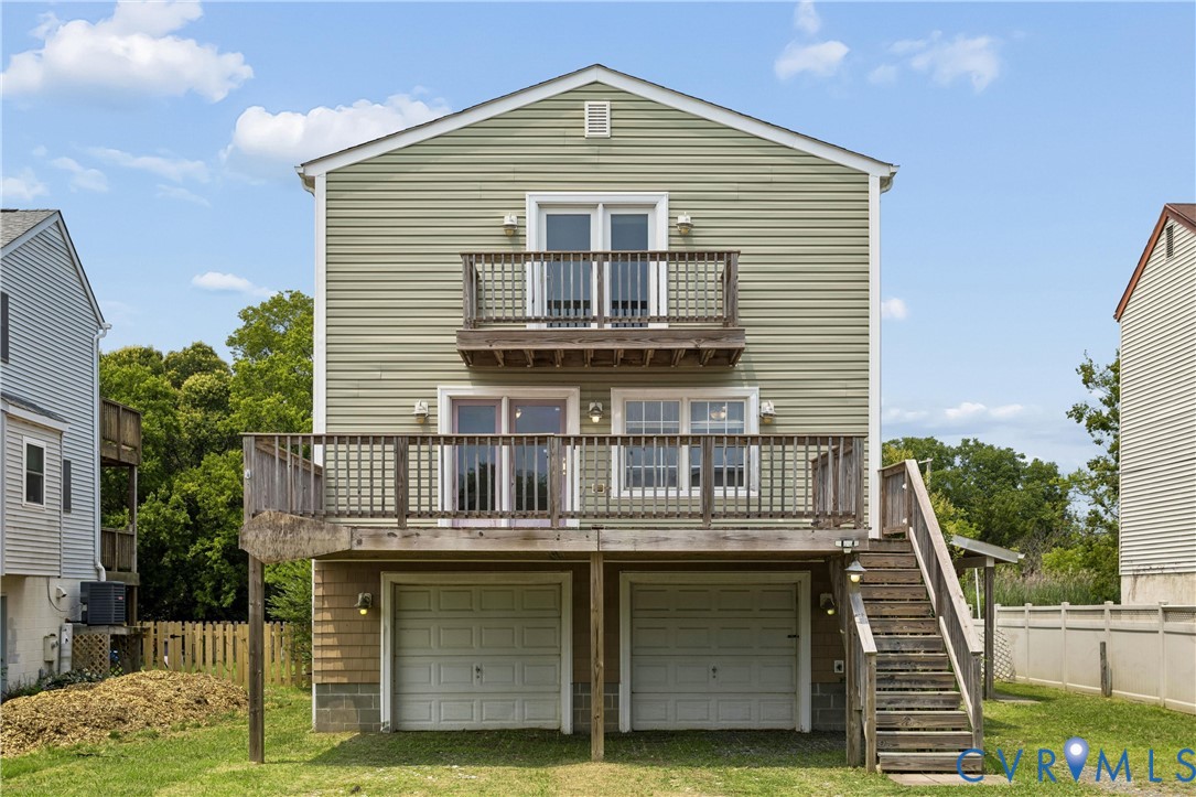 Rear exterior featuring light green horizontal siding, two-car garage, elevated wood deck with stairs, and private balcony Rear exterior featuring light green horizontal siding, two-car garage, elevated wood deck with stairs, and private balcony