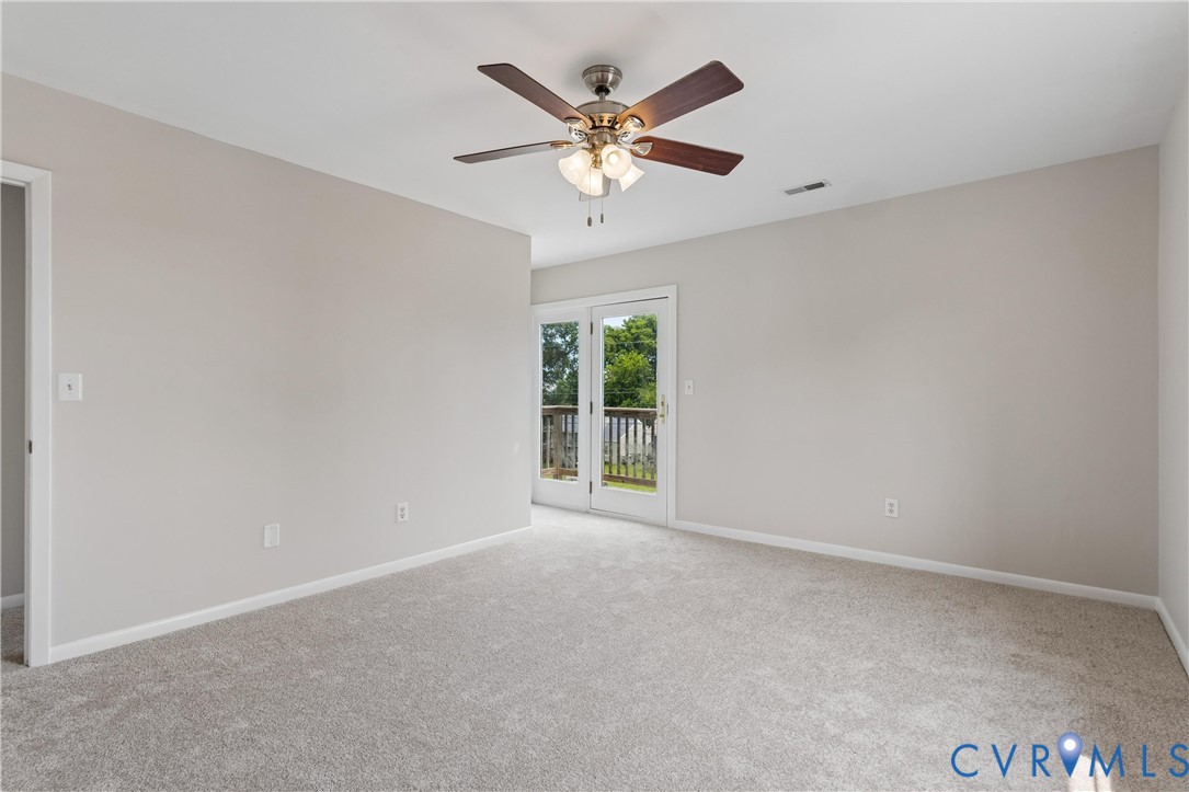 Neutral-toned interior space featuring carpeting, a multi-blade ceiling fan with integrated light fixture, and glass-paneled double doors providing outdoor access