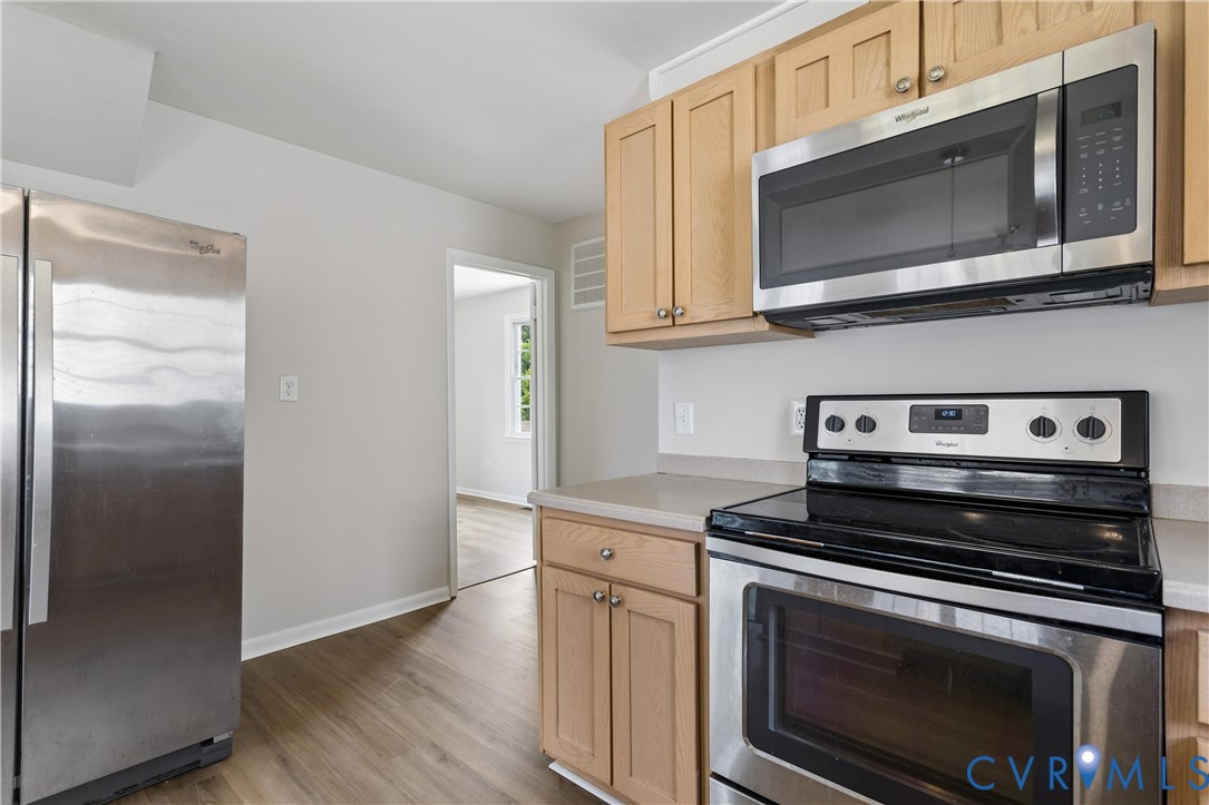 Kitchen featuring natural wood-finish cabinetry, stainless steel appliances, solid surface countertops, and wood-finish flooring