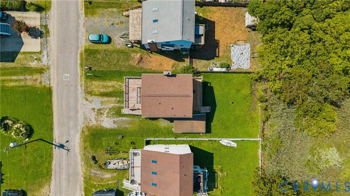 Aerial perspective featuring an expansive rear lawn, elevated wooden deck, and a multi-level structure with a gabled roof