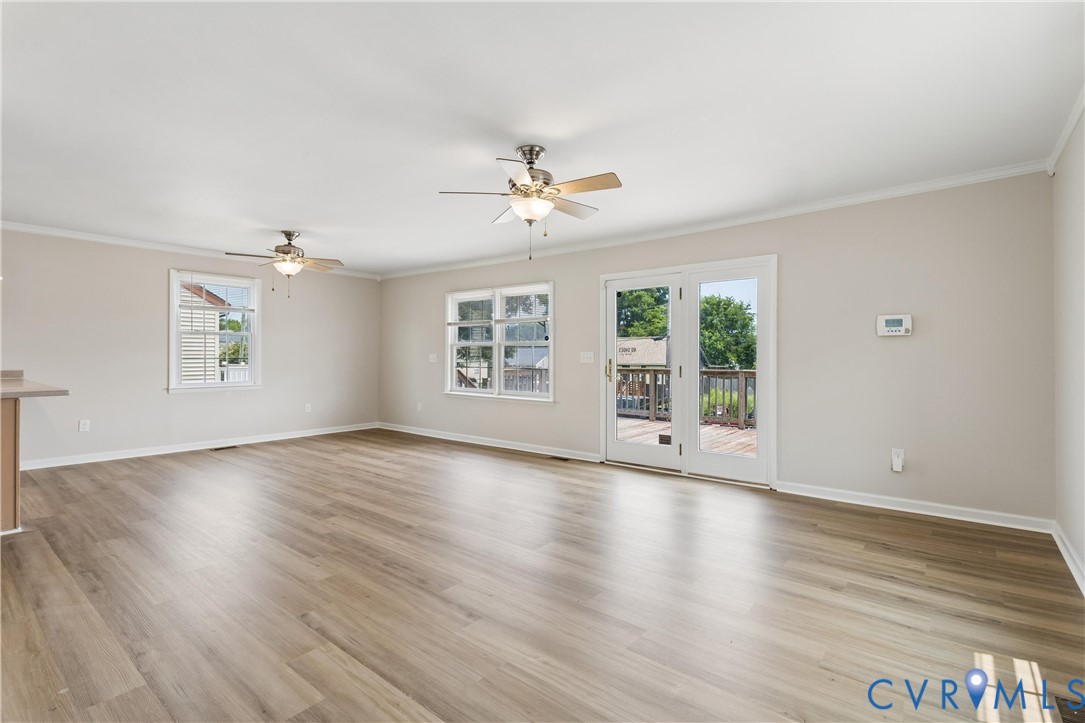 Spacious interior featuring wood-finish flooring, dual ceiling fans, crown molding, and glass-paneled double doors Spacious interior featuring wood-finish flooring, dual ceiling fans, crown molding, and glass-paneled double doors
