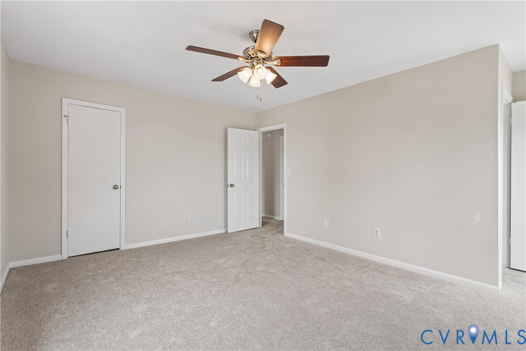 Neutral-toned interior space featuring neutral carpeting, a ceiling-mounted fan with integrated lighting, and multi-panel interior doors