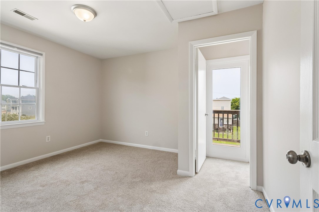 Neutral wall tones, carpeted flooring, multi-pane window, flush-mount ceiling lighting, and door providing outdoor access