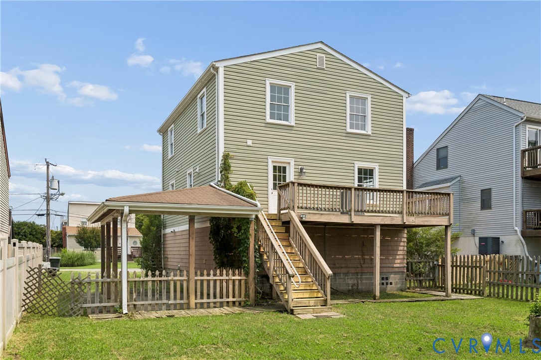Exterior featuring green vinyl siding, an elevated wood deck with railing, a covered ground-level patio, a wooden staircase, and a fenced yard