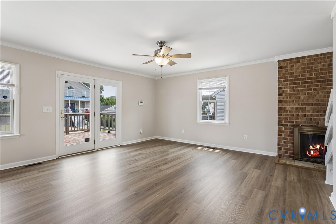 Living area featuring wood-finish flooring, a brick fireplace with a built-in insert, double-pane windows, and double-glass doors opening to an exterior deck