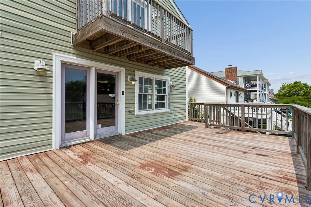 Exterior wood deck with railings, horizontal siding, double-door entry, and a second-level balcony